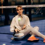 Een man in lange padelbroeken speelt padel op de baan, met een padelracket in de hand.