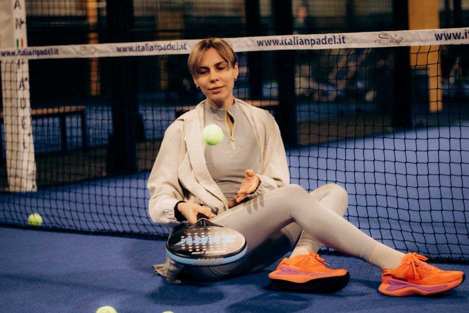 Een man in lange padelbroeken speelt padel op de baan, met een padelracket in de hand.
